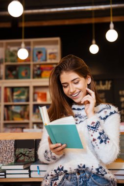 Kitap okuma ve cep telefonu üzerinde konuşurken gülümseyen genç kadın