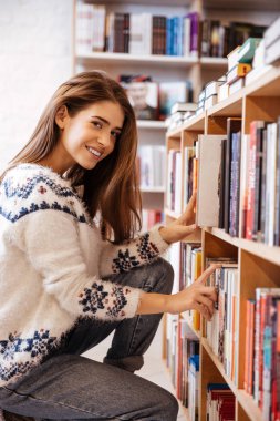 Kitaplığındaki kitap raf kitaplarda arayan kadın