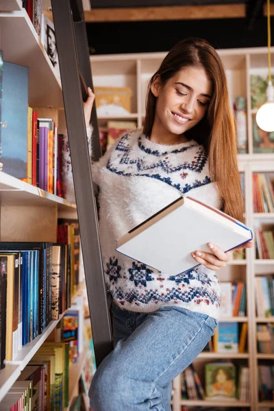 Studentin holt Buch aus Regal in Bibliothek — Stockfoto