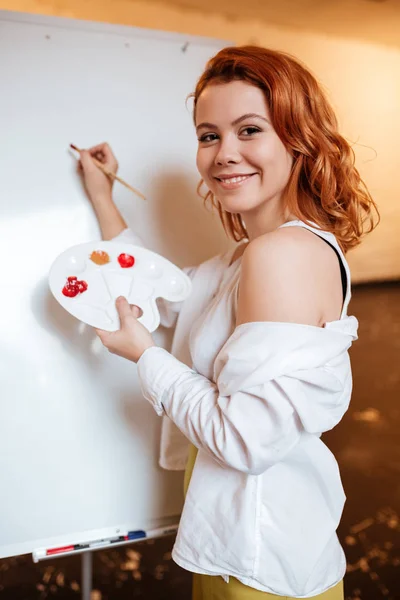 Sorrindo bela mulher pintor pintura com tintas a óleo em branco — Fotografia de Stock