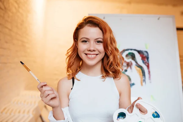 Wanita pelukis gembira dengan rambut merah berdiri di atas kanvas kosong — Stok Foto