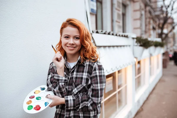 Cheerful young lady painter with red hair walking on street — Stock Photo, Image