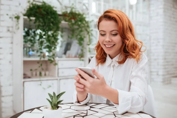 Bella rossa giovane donna chatta dal suo telefono in caffè — Foto Stock