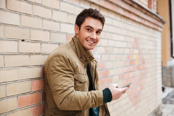 Glimlachend jongeman chatten zijn telefonisch buitenshuis — Stockfoto
