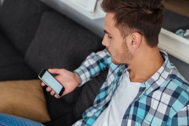 Evde kanepede oturan ve seyir telefon bir adam.