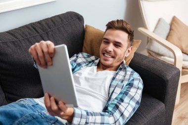 Kanepe ve tablet bilgisayarda çalmayı kıl adam yatıyor