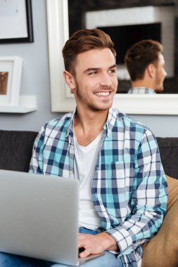 Kanepede oturan ve dizüstü bilgisayar kullanarak neşeli kıl adam