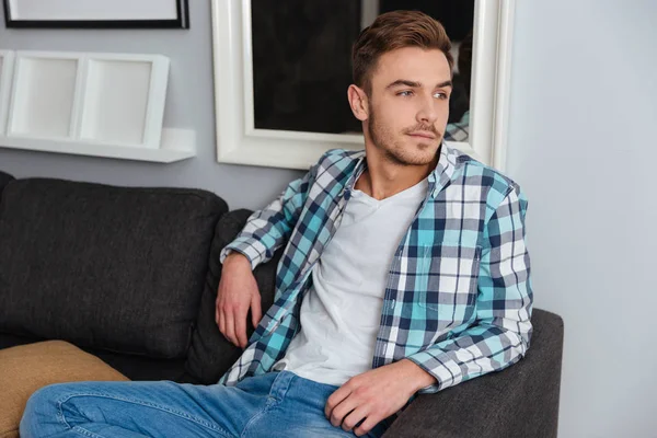 Guapo joven sentado en el sofá en casa — Foto de Stock