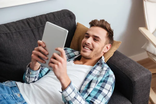 Hombre cerda alegre se encuentra en el sofá y el uso de la computadora de tableta — Foto de Stock