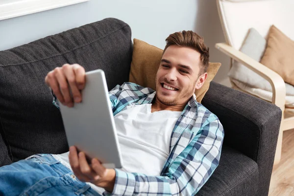 Borst man ligger på soffan och spelar på tablet PC — Stockfoto