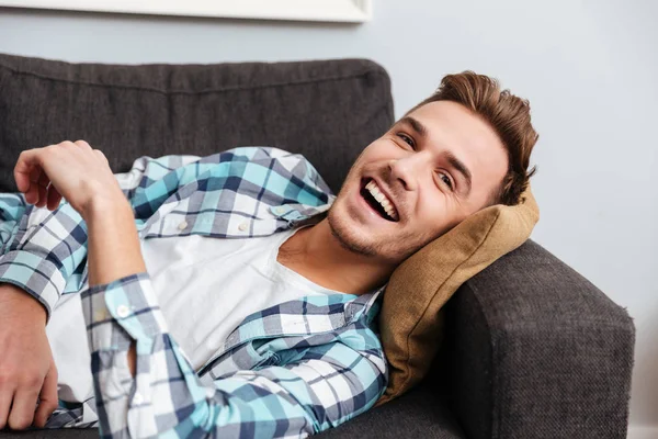 Щасливий молодий чоловік лежить на дивані і дивиться вбік . — стокове фото
