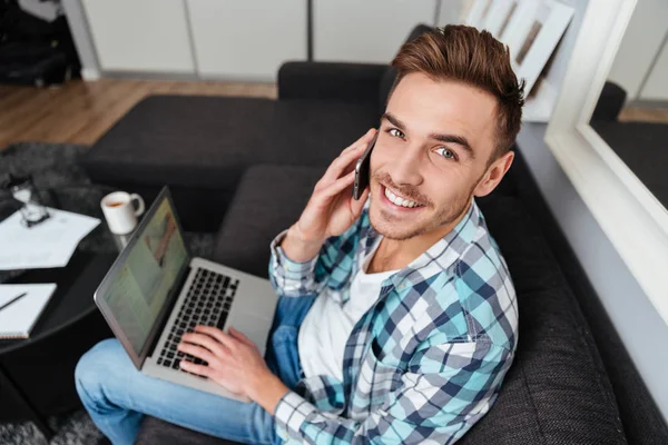 Vrolijke man met laptop tijdens een gesprek zijn telefonisch. — Stockfoto