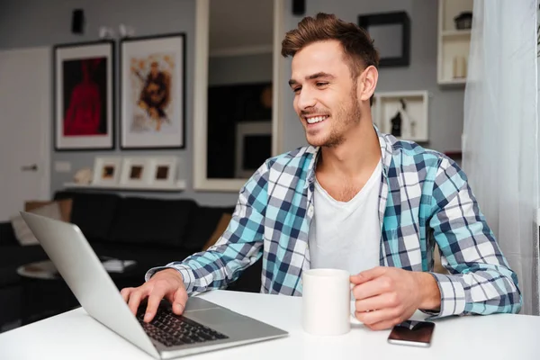 Lachen jongeman laptopcomputer gebruikt terwijl het drinken van thee. — Stockfoto