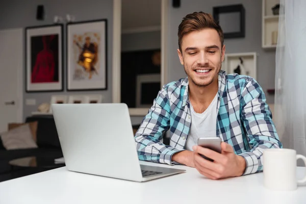 Hombre alegre usando el teléfono móvil y el ordenador portátil . — Foto de Stock