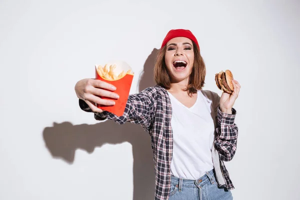 Mujer emocional sosteniendo papas fritas y hamburguesa — Foto de Stock