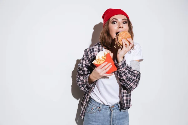 Mujer joven hambrienta comiendo papas fritas y hamburguesa —  Fotos de Stock