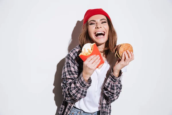 Hambrienta mujer riendo sosteniendo papas fritas y hamburguesa —  Fotos de Stock