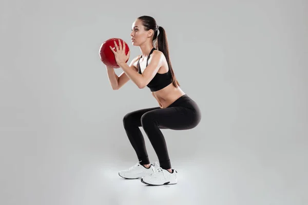 Привлекательная молодая спортсменка делает приседания с медицинским мячом — стоковое фото
