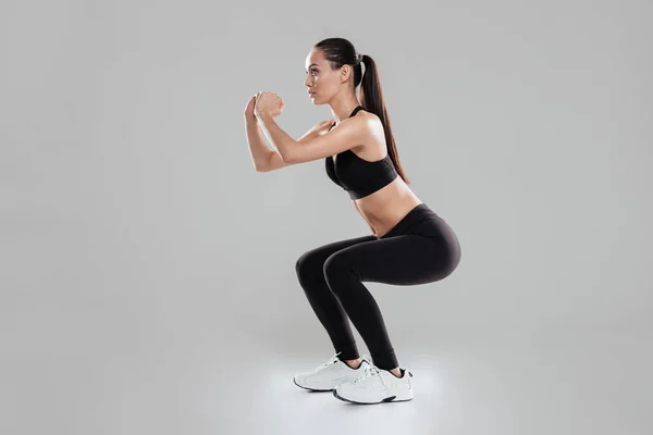 Full length of concentrated young woman athlete doing squats — Stock Photo, Image