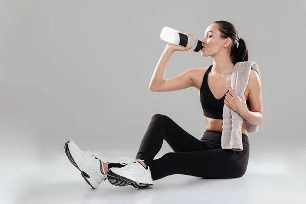 Relaxed young fitness woman with towel sitting and drinking water — Stock Photo, Image