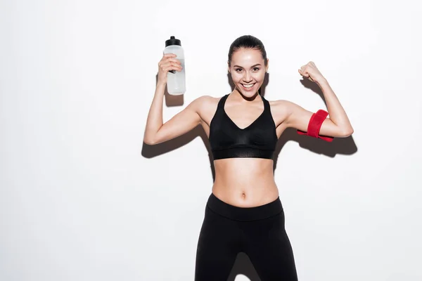 Happy young woman athlete with bottle of water showing biceps — Stock Photo, Image