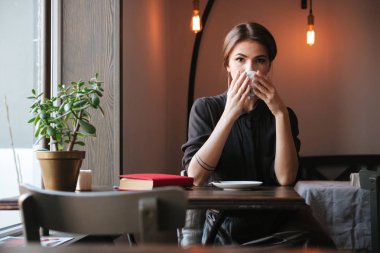 Çekici genç kadın kahve yudumlarken oturuyordu.