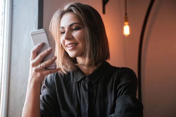 Cheerful young woman in cafe chatting by her phone. — Stock Photo, Image