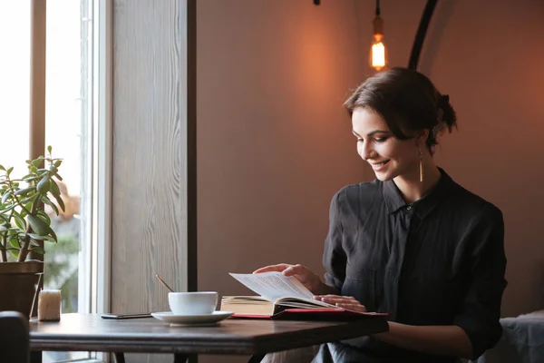 Улыбающаяся молодая женщина читает книги в кафе — стоковое фото
