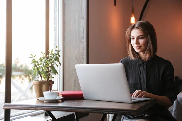 Hübsche junge Frau sitzt im Café und schaut auf Laptop — Stockfoto
