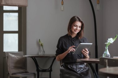 Tablet bilgisayar kullanarak pencere oturan neşeli Bayan.