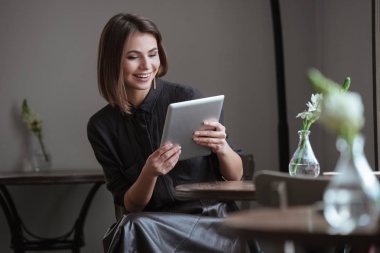 Tablet bilgisayar kullanarak pencere oturan güzel kadın.