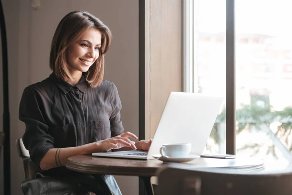 Glada damen sitter vid bord i café och använder bärbar dator. — Stockfoto