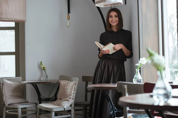 Bela senhora de pé perto da janela no café e livro de leitura . — Fotografia de Stock