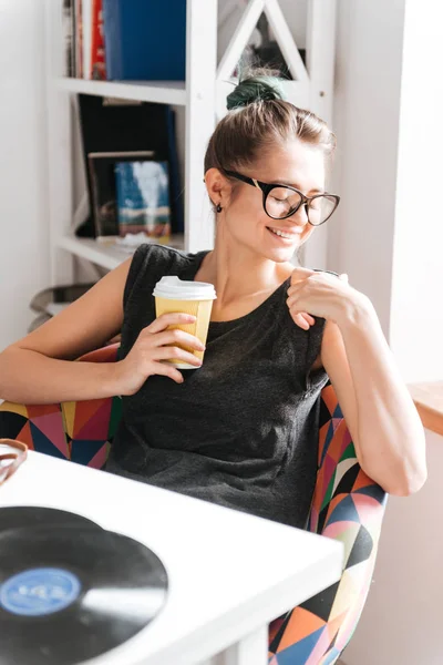 Usměvavá mladá žena sedí u stolu a pití kávy — Stock fotografie
