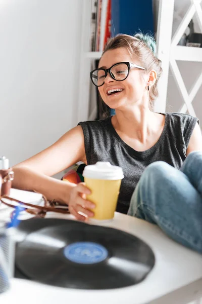 Glad ung kvinna sitter med benen på bordet och skrattar — Stockfoto