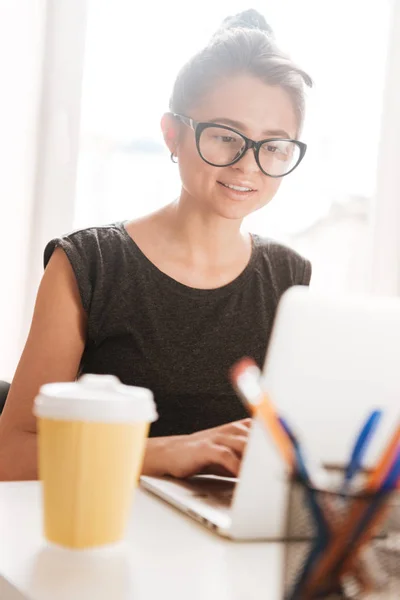 Concentrated woman in glasses drinking coffee and working with laptop — Stock Photo, Image