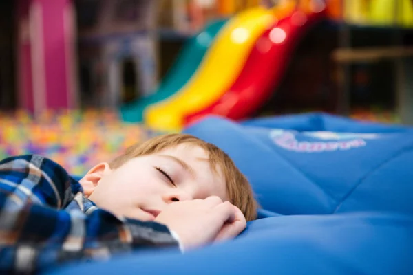 Fáradt, kimerült kisfiú alszik, fedett vidámpark — Stock Fotó