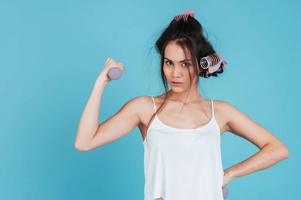 Portrait of a serious young woman with curlers doing exercises — Stock Photo, Image