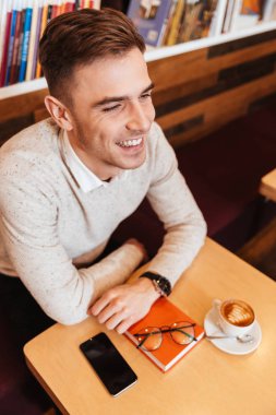 Fincan kahve ve kitap ile kafede oturan adam.