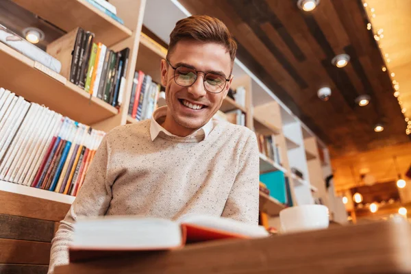 Jovem homem alegre sentado no café enquanto lê o livro . — Fotografia de Stock
