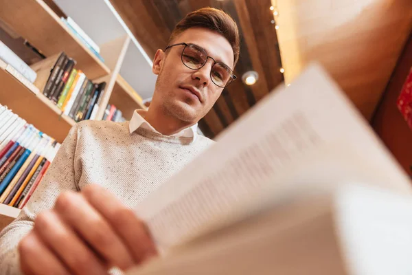 Giovane uomo concentrato seduto nel caffè durante la lettura del libro . — Foto Stock