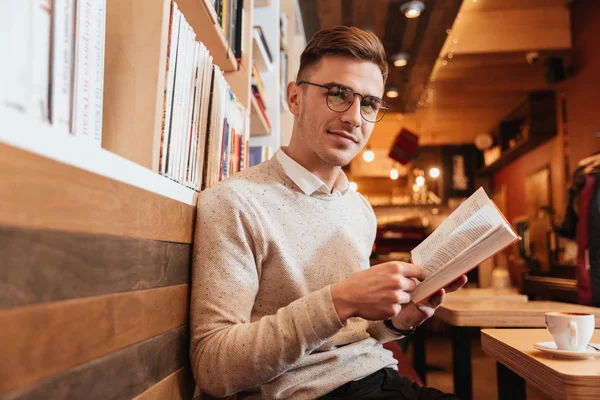 Hombre alegre sentado en la cafetería mientras lee el libro — Foto de Stock