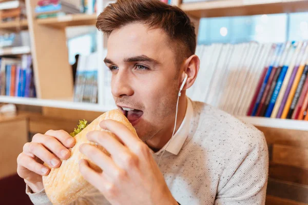 Young hungry man eating sandwich and listening music. — Stock Photo, Image