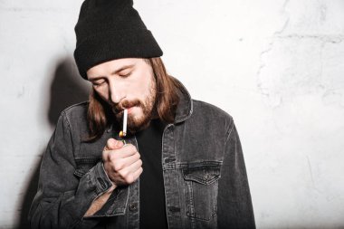 Sigara ile ayakta şapka giyen çekici hipster adam