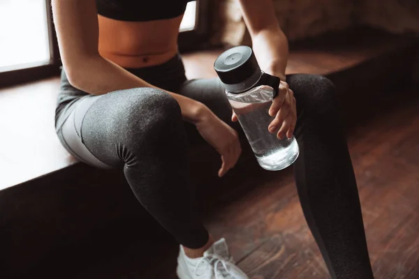 Attractive fitness woman sitting in gym and holding water. — Stock Photo, Image