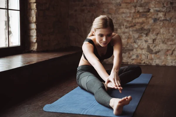 Ganska ung fitness kvinna sitter och stretching hennes ben — Stockfoto