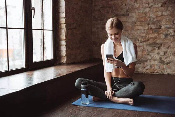 Fitness kvinna med handduk sitter i gymmet medan du använder telefonen — Stockfoto