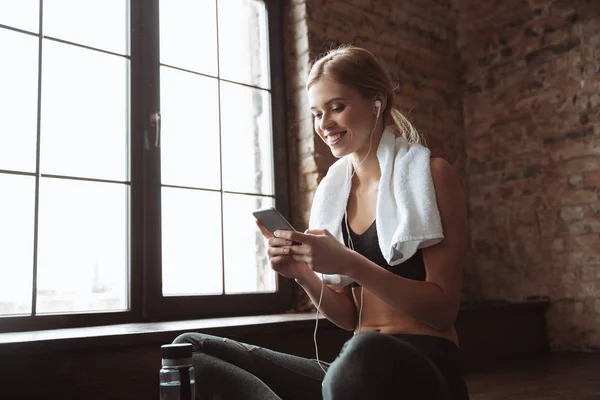 Chica de fitness con toalla sentada en el gimnasio mientras escucha música . — Foto de Stock