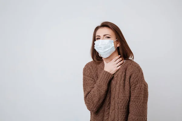 Woman in sweater and medical mask holding her neck — Stock Photo, Image