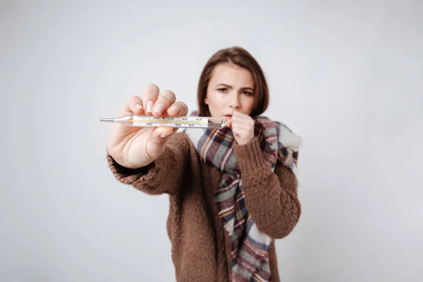 Syg kvinde i sweater og tørklæde viser termometer - Stock-foto